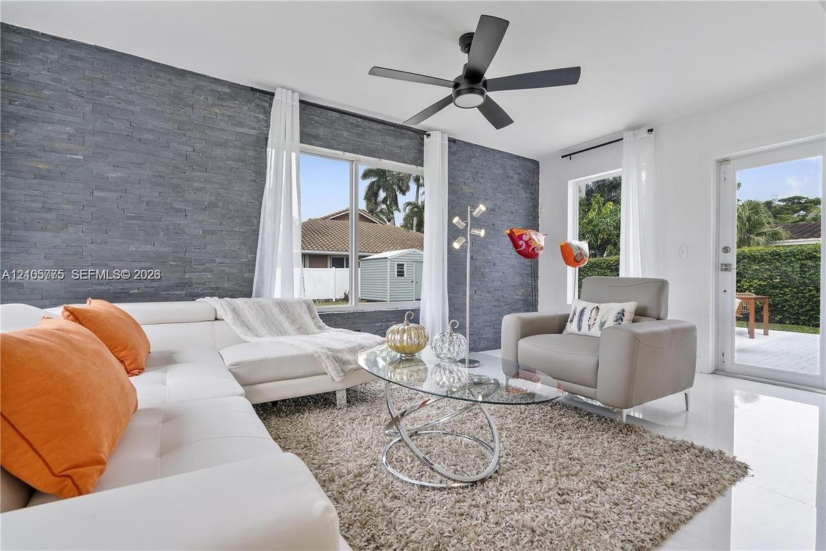 Living area featuring a floor-to-ceiling charcoal stone veneer accent wall, large picture windows, matte black ceiling fan with integrated lighting, a