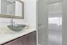 Bathroom vanity featuring a dark-finish wood cabinet, solid-surface countertop, glass vessel sink, and a framed wall mirror, accompanied by a glass-en