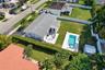 Aerial perspective of a property featuring an in-ground swimming pool, paved patio, expansive lawn, white vinyl perimeter fencing, and a detached stor