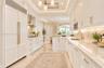 Kitchen featuring custom white cabinetry, integrated panel-ready refrigerator, stone countertops, under-cabinet lighting, and tray ceiling with recess