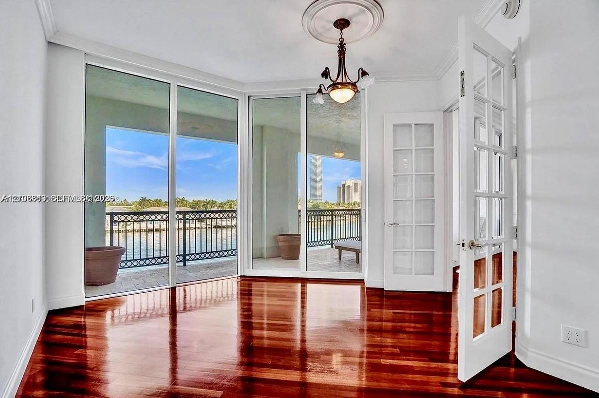 Room featuring polished wood-finish flooring, floor-to-ceiling glass paneling, a decorative ceiling medallion with an attached chandelier, and French-