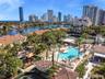 Waterfront community featuring an expansive swimming pool, professional-grade tennis courts, mature tropical landscaping, and tile-roof architecture
