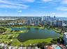 Aerial perspective featuring an expansive lake, manicured golf course greens, sand bunkers, mature landscaping, and coastal high-rise structures