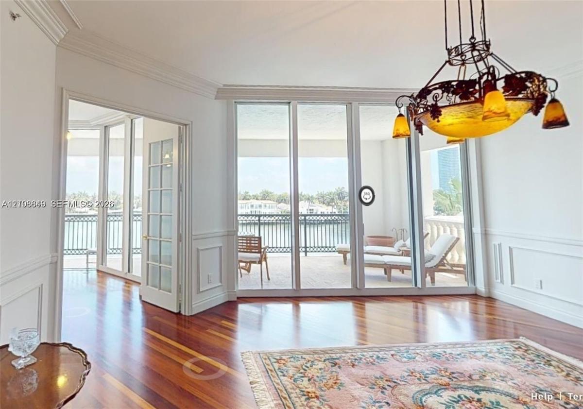 Room featuring wood-finish flooring, wainscoting, intricate crown molding, a decorative metal chandelier, and floor-to-ceiling glass panel doors