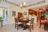 Open-concept dining area featuring stone tile flooring, stained wood cabinetry, recessed lighting, a decorative chandelier, and a full-glass exterior 
