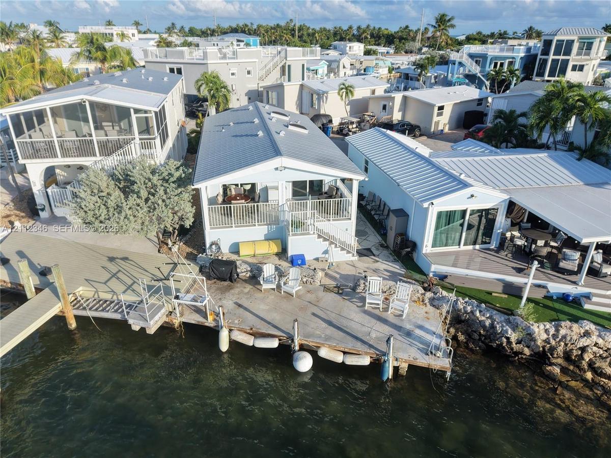 Waterfront residence featuring a metal roof, skylights, raised balcony with metal railings, and a concrete bulkhead with an attached private dock