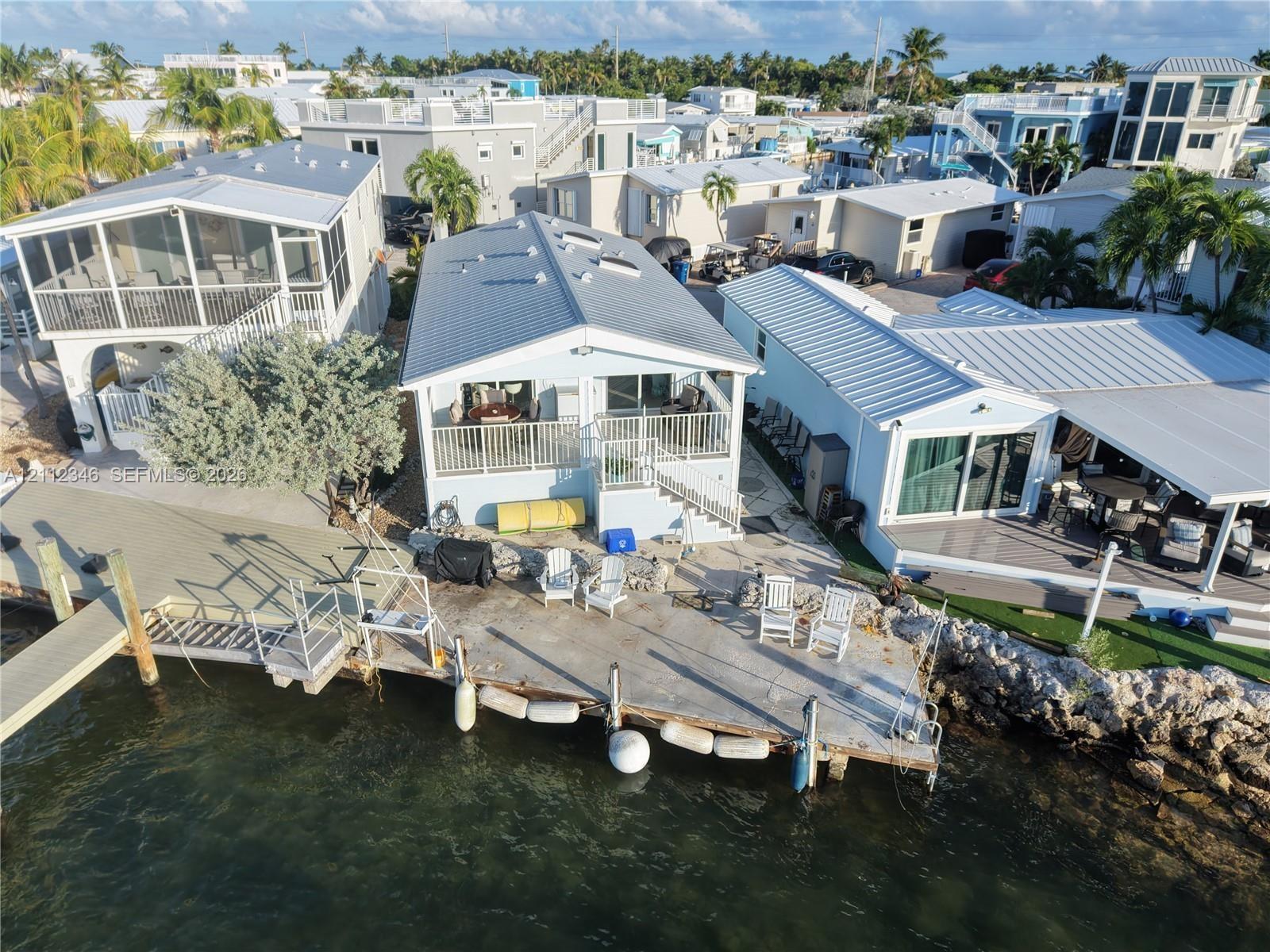 Waterfront residence featuring a metal roof, skylights, raised balcony with metal railings, and a concrete bulkhead with an attached private dock
