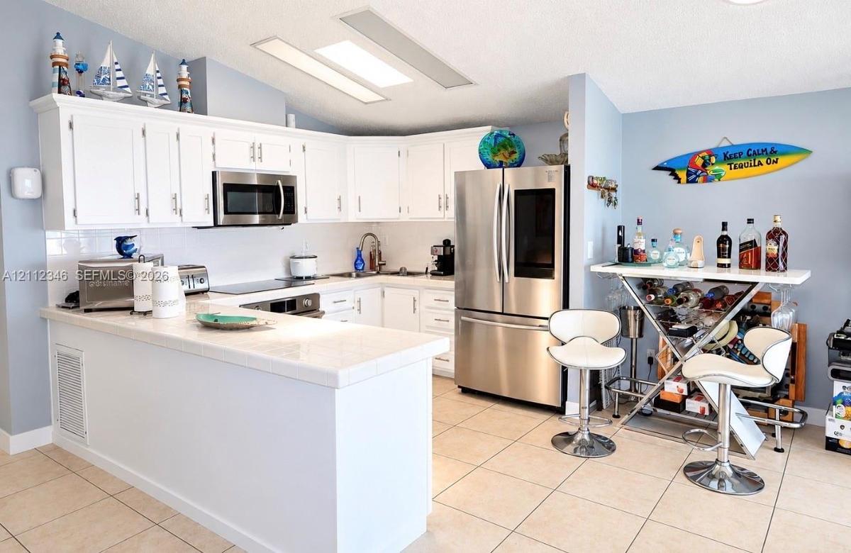 Kitchen featuring white cabinetry, tile countertops, stainless steel appliances, and tile flooring