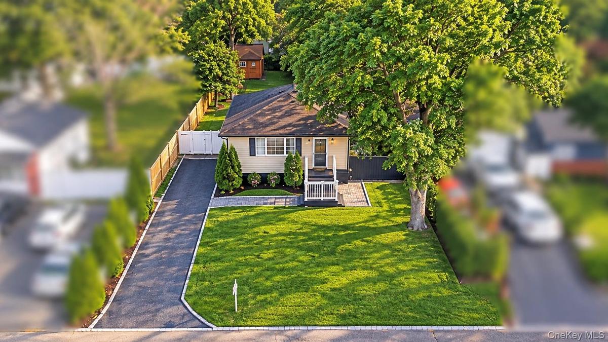 Single-story residence featuring a paved driveway, manicured lawn, stone-paver walkway, wood-fencing, and mature landscaping
