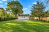 Backyard featuring a manicured lawn, concrete patio, perimeter wood fencing, mature trees, and privacy-screening shrubbery
