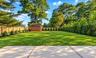 Expansive backyard featuring a concrete patio, manicured lawn, detached storage shed, perimeter wood fencing, and mature evergreen privacy hedging