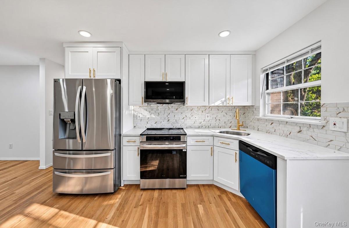 Kitchen featuring white shaker-style cabinetry, stainless steel appliances, stone-look countertops, patterned tile backsplash, and wood-finish floorin