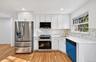 Kitchen featuring white shaker-style cabinetry, stainless steel appliances, stone-look countertops, patterned tile backsplash, and wood-finish floorin