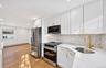 Kitchen featuring white shaker-style cabinetry with gold-tone hardware, stone-surface countertops, decorative tile backsplash, wood-finish flooring, a