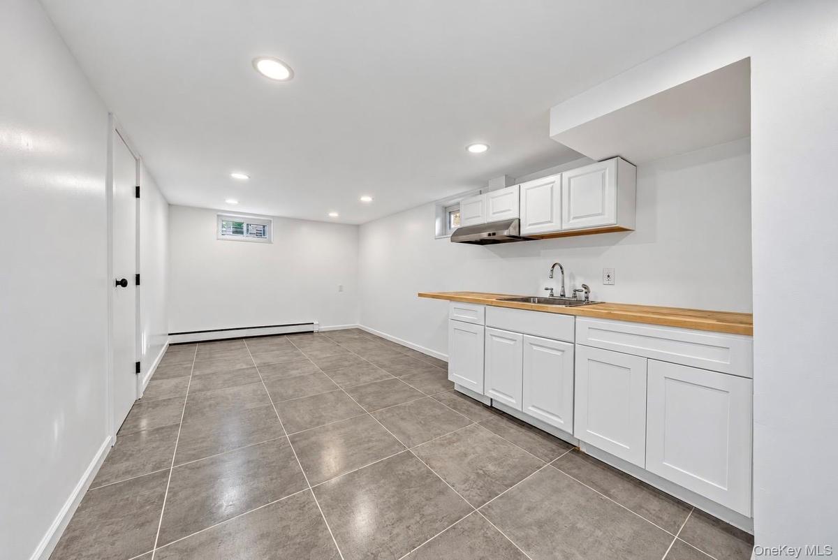 Kitchenette area featuring white shaker-style cabinetry, wood-finish countertops, stainless steel sink, recessed lighting, and tile flooring