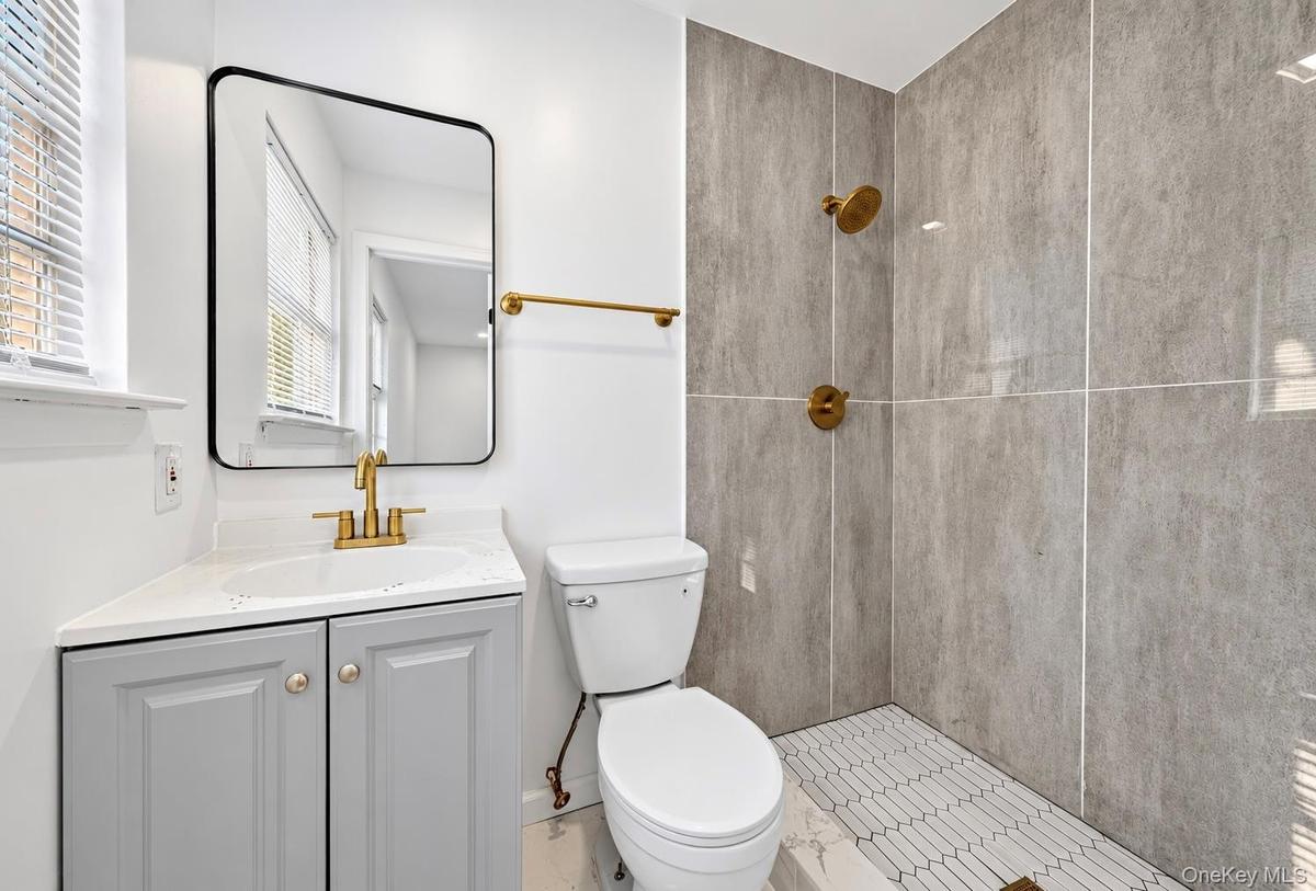 Bathroom featuring a grey vanity cabinet with a white countertop, brushed gold plumbing fixtures, a rectangular vanity mirror with a black frame, and 