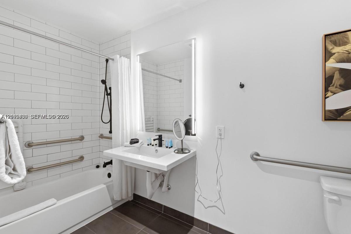 Wall-mounted floating vanity with integrated sink, rectangular illuminated mirror, white subway-tiled shower surround, matte black plumbing fixtures, 