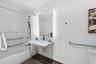 Wall-mounted floating vanity with integrated sink, rectangular illuminated mirror, white subway-tiled shower surround, matte black plumbing fixtures, 