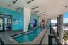 Covered outdoor pool featuring grey stone-finish tile decking, structural concrete support columns, a glass railing system, and linear recessed lighti