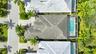 Aerial perspective featuring a multi-hipped roofline, paved driveway, and a screened-in pool enclosure
