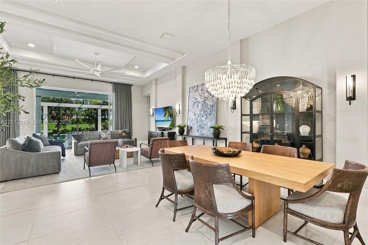 Open-concept living space featuring high tray ceilings, recessed lighting, expansive tile flooring, and a crystal chandelier
