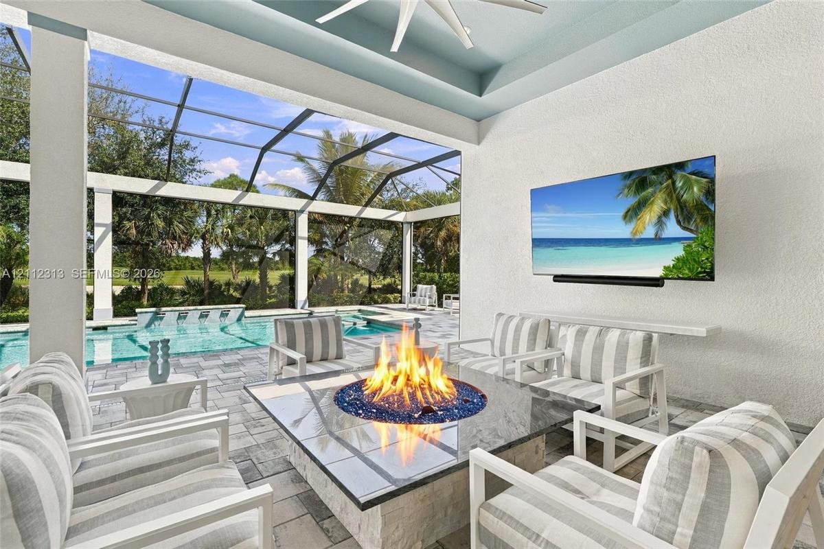 Covered lanai featuring a stone-topped built-in fire pit, screened enclosure, custom ceiling fan, and built-in wall-mounted television, accented by pa