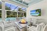 Covered lanai featuring a stone-topped built-in fire pit, screened enclosure, custom ceiling fan, and built-in wall-mounted television, accented by pa
