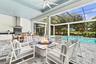 Covered outdoor living area featuring a built-in kitchen with stainless steel range hood, stone-clad fire feature, paver flooring, and a screened-in s