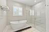 Freestanding soaking tub with chrome fixtures, glass-enclosed walk-in shower with floor-to-ceiling tile, and window shutters