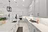 Kitchen featuring light-toned cabinetry, a spacious island with a built-in sink, stone-finish countertops, stainless steel appliances, and a geometric