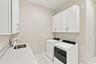 Laundry area featuring white shaker-style wall cabinets, a light-toned countertop, an integrated stainless steel sink with a chrome faucet, and wood-f