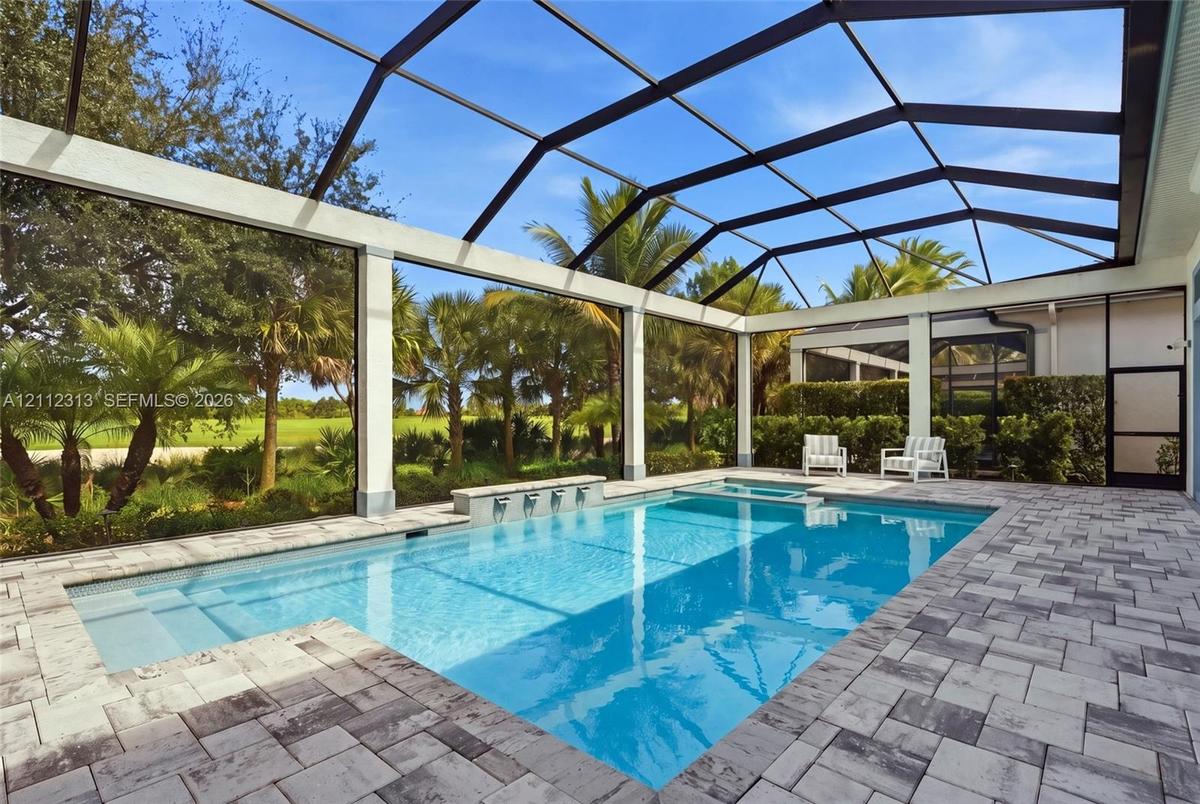 Screened pool enclosure featuring a stone-paver deck, built-in spa, and a wall fountain with multiple spillway spouts