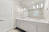 Double vanity featuring light-toned cabinetry, stone-finish countertops, undermount sinks, polished metal fixtures, and a wall-to-wall mirror with mul