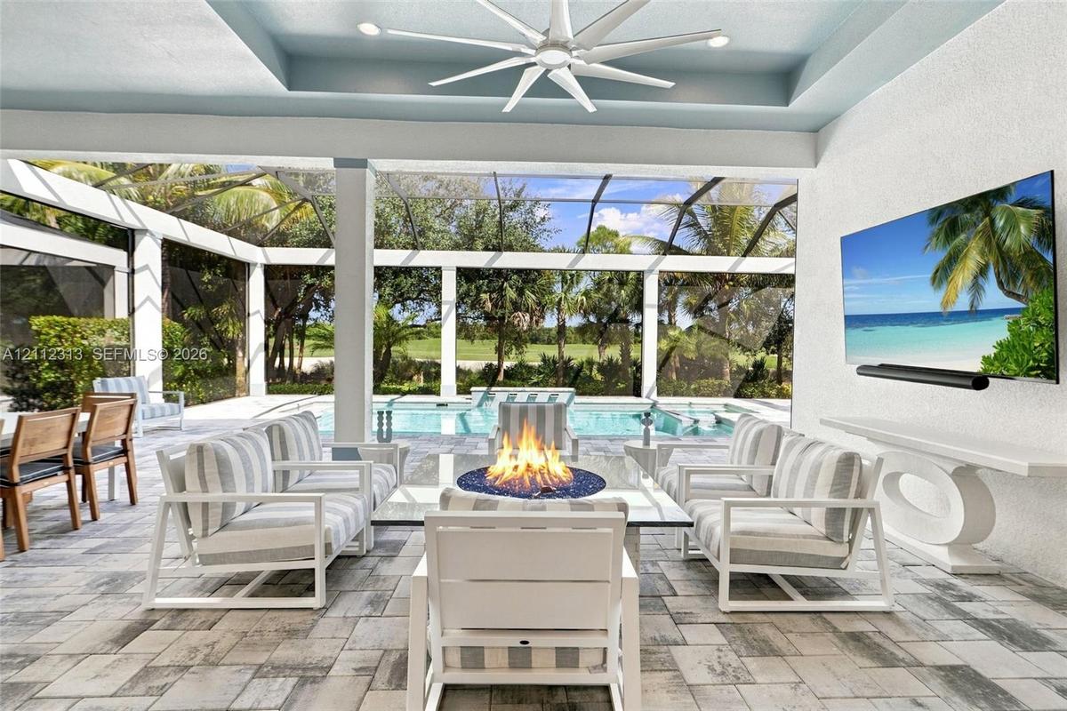 Covered outdoor living space featuring a recessed tray ceiling, multi-blade ceiling fan, paver flooring, built-in wall-mounted television, and a scree