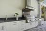 Outdoor kitchen featuring white shaker-style cabinetry, dark natural stone countertops and backsplash, stainless steel built-in grill, commercial-grad