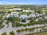 Aerial perspective of a multi-winged facility featuring a central clock tower, expansive pond frontage, mature palm tree landscaping, and paved circul