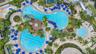 Aerial view of a sprawling pool complex featuring multiple swimming pools, a dedicated lap lane section, a central gazebo, and expansive paved decking