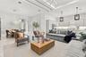 Open-concept living space featuring high tray ceilings, recessed lighting, neutral tile flooring, modern pendant light fixtures, and white cabinetry
