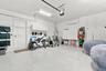 Garage featuring epoxy-coated flooring, wall-mounted white storage cabinetry, an installed climate control unit, and an automated garage door opener s