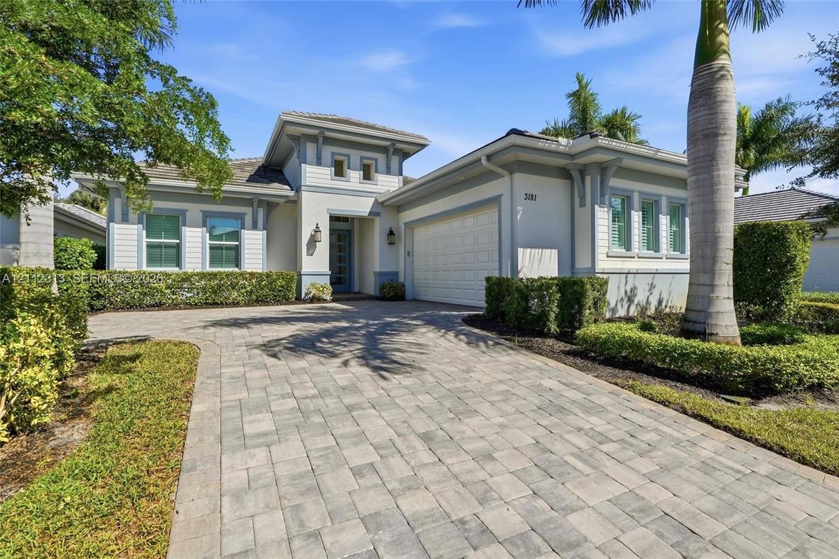Single-story residence featuring a neutral stucco exterior, paver driveway, multi-pane windows, and a multi-tiered roofline with decorative corbels