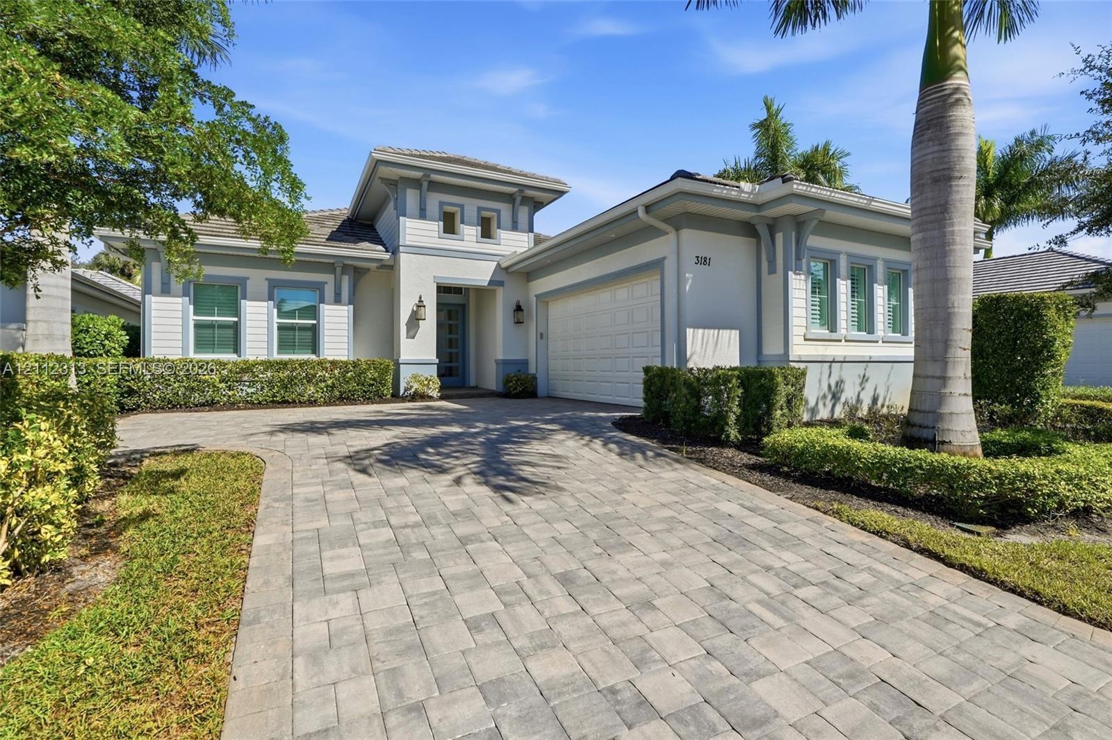Single-story residence featuring a neutral stucco exterior, paver driveway, multi-pane windows, and a multi-tiered roofline with decorative corbels