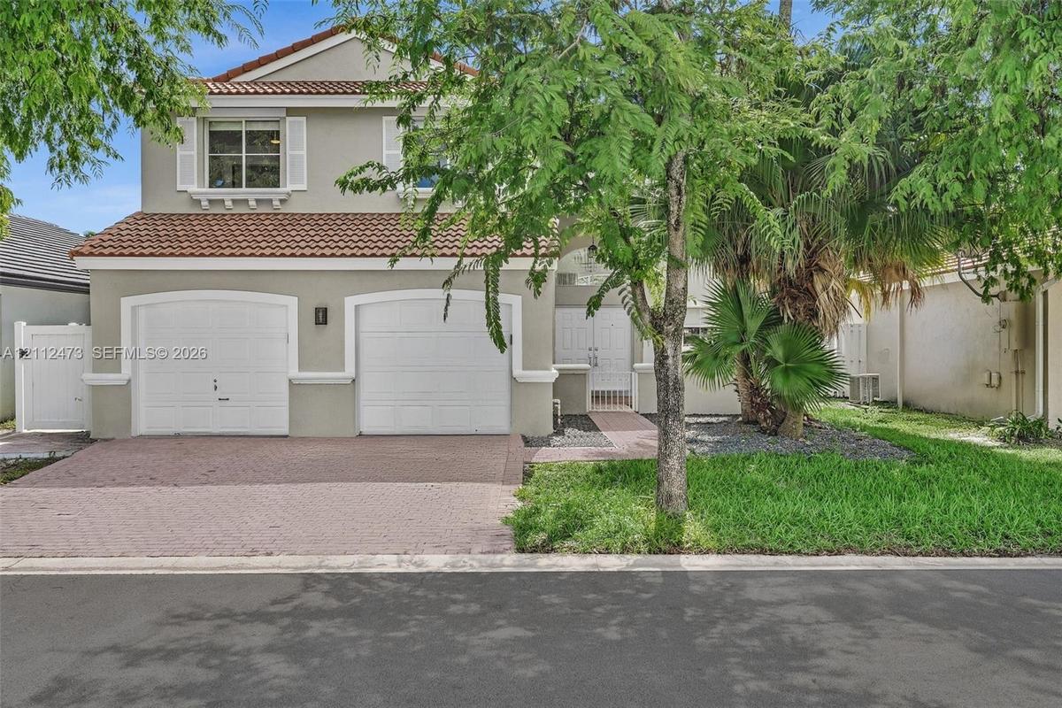 Two-story residence featuring a tile roof, dual-bay garage, paved driveway, and double-entry doors