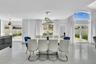 Open-concept interior featuring large-format tile flooring, a contemporary multi-ring crystal chandelier, vaulted ceilings, and dual sets of glass-pan