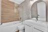 Bathroom featuring a floating white vanity with a rectangular sink, arch-top mirror, wood-finish wall tile, frameless glass shower panel, and large-fo
