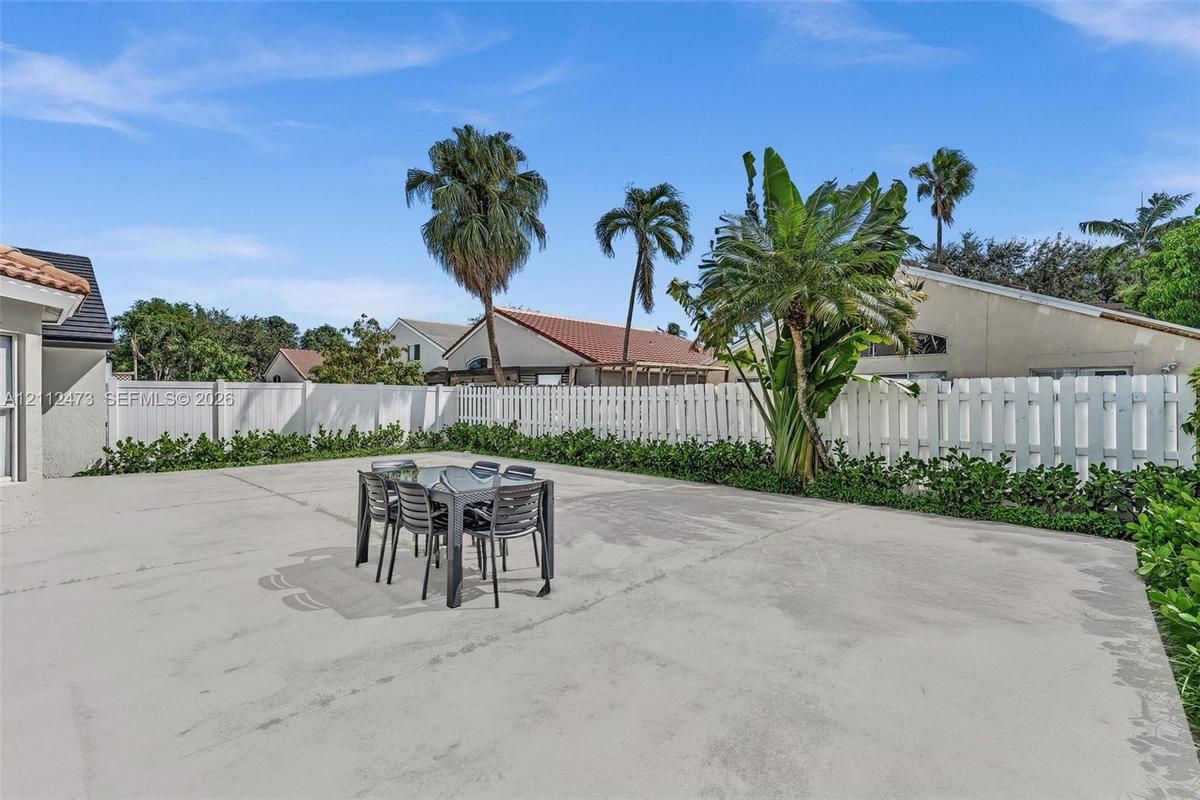 Expansive concrete patio area enclosed by a white vinyl privacy fence, featuring mature palm trees and established perimeter landscaping