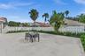 Expansive concrete patio area enclosed by a white vinyl privacy fence, featuring mature palm trees and established perimeter landscaping