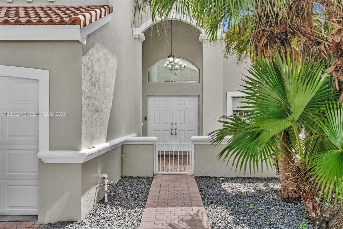 Stucco exterior featuring an arched entryway, double-door entrance, red tile roofing, decorative chandelier, and a paved walkway