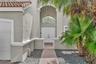 Stucco exterior featuring an arched entryway, double-door entrance, red tile roofing, decorative chandelier, and a paved walkway