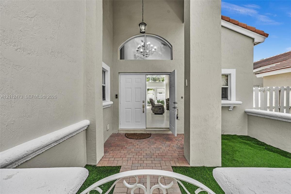 Stucco entryway featuring a covered porch, brick paver flooring, arched transom window, and an attached lantern-style pendant light