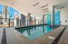 Covered swimming pool featuring large-format tile decking, structural concrete columns, a sleek glass railing, and linear ceiling lighting